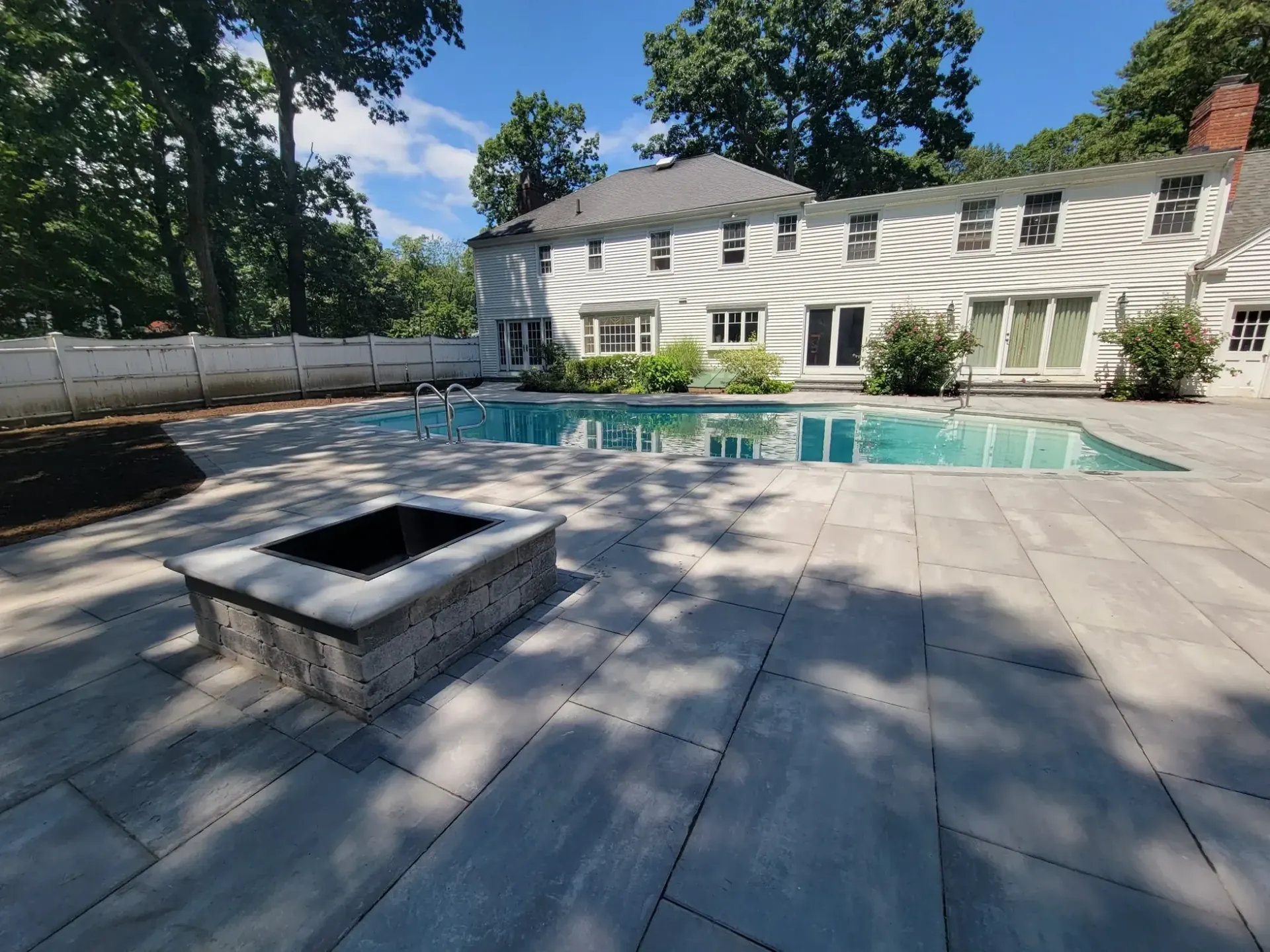 Large-format paver pool deck with a square block fire pit, built by Gerrior in Lynnfield, MA